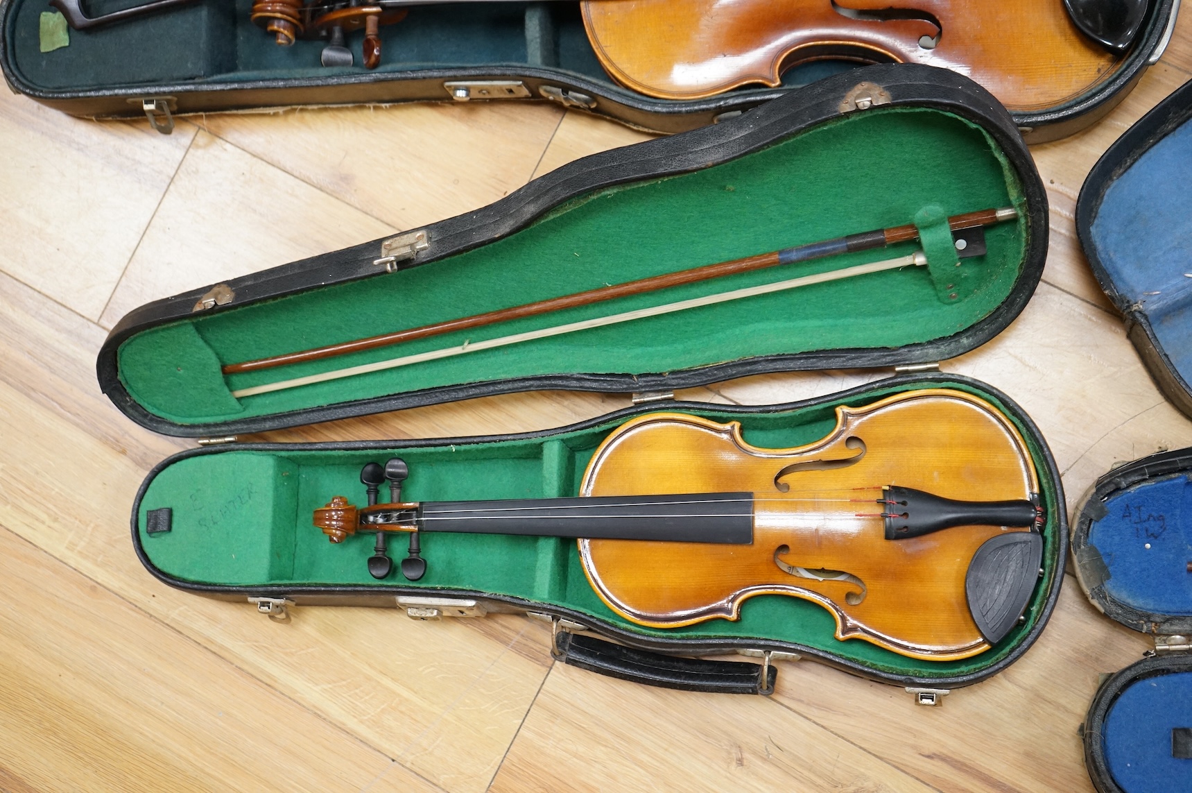 Five cased 20th century violins, including; a German violin, two Czech violins, a three-quarter size violin with a label for Bienfait, and a Romanian quarter size violin, all in cases or the remains of cases.
